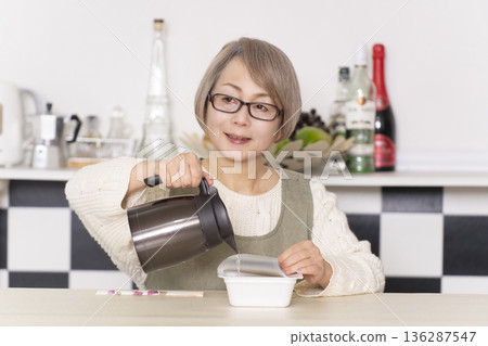 廚房裡,一位老婦人正往杯麵倒熱水。 廚房裡,一位老婦人正往杯麵倒熱水。 136287547