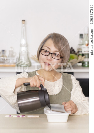 廚房裡,一位老婦人正往杯麵倒熱水。 廚房裡,一位老婦人正往杯麵倒熱水。 136287553