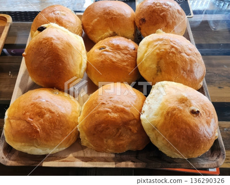 Freshly Baked Golden Brown Raisin Buns on a Rustic Wooden Serving Tray 136290326