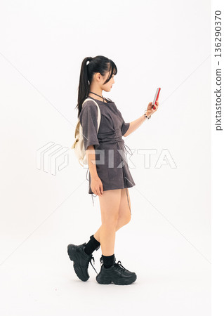 Full-body photo of a teenage woman walking while looking at her smartphone Full-body photo of a teenage woman walking while looking at her smartphone 136290370