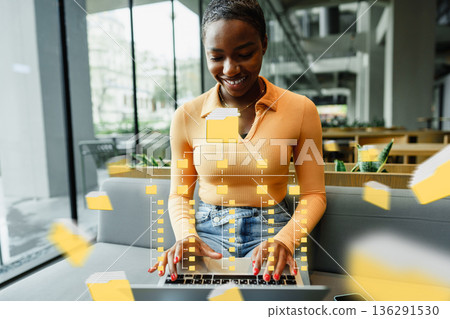 Woman uses laptop in office with digital elements floating around 136291530