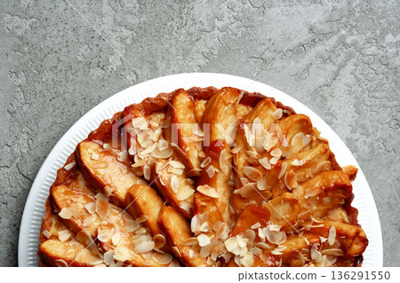 Delicious baked apple tart with almond slices on white plate against gray background Delicious baked apple tart with almond slices on white plate against gray background 136291550