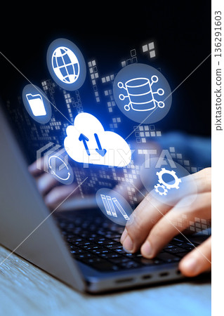 Hands using a laptop with cloud computing icons in a dark setting 136291603