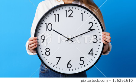 Holding a large clock showing the time and a blue background Holding a large clock showing the time and a blue background 136291610