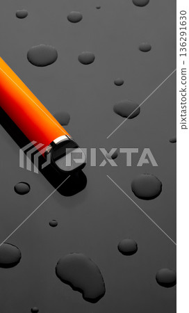 Close-up of an orange pen on a black surface with water droplets at midday 136291630