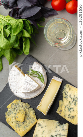 Cheese platter with greens, tomatoes, and glass of white wine on a table Cheese platter with greens, tomatoes, and glass of white wine on a table 136291650