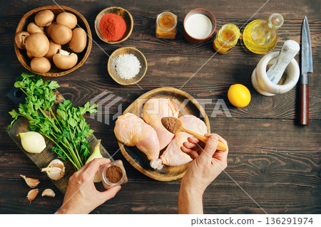 Hands seasoning raw chicken legs with spice on rustic wooden table with ingredients 136291974