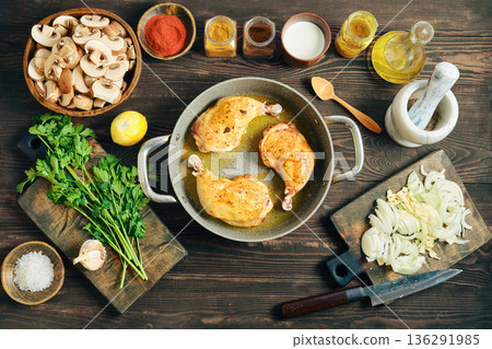 Fried seasoned chicken legs in a pan on a wooden table with chopped ingredient 136291985