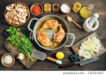 Cooking chicken legs with mushrooms and onions in a kitchen with various ingredients on the table 136291987