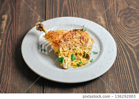 Cooked chicken leg served on a plate with creamy sauce and herbs during a meal preparation time 136292003