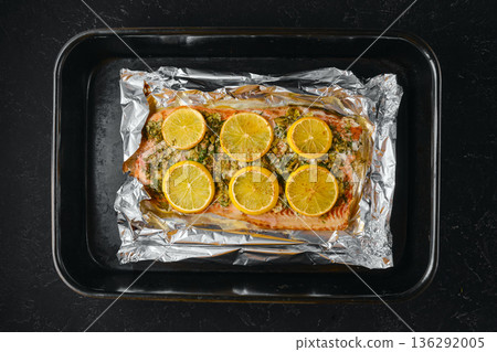 Cooking pink salmon with lemon slices on a baking sheet lined with foil in the kitchen 136292005