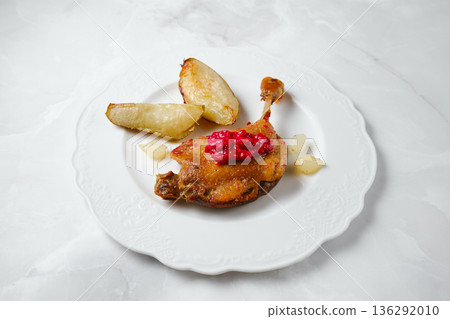 Duck confit served on a plate with potato wedges and red sauce at a dining table Duck confit served on a plate with potato wedges and red sauce at a dining table 136292010