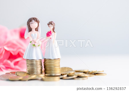 Inclusive wedding savings concept with two bride figurines on stacked coins, pastel pink flowers and copy space, celebrating diversity, equality, shared financial planning for couples. wedding savings Inclusive wedding savings concept with two bride figurines on stacked coins, pastel pink flowers and copy space, celebrating diversity, equality, shared financial planning for couples. wedding savings 136292837