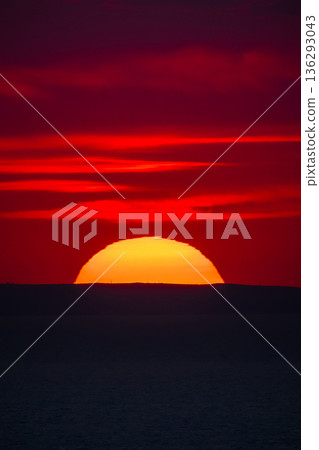 Sunset over the sea horizon with a dark silhouette of distant hills. 136293043