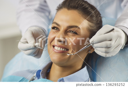 Happy patient at dental clinic receiving routine checkup with mirror and scaler 136293252