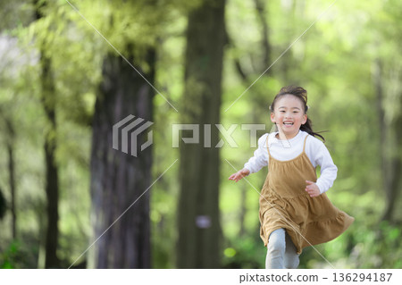 一個快樂的孩子，捕捉女孩在綠樹成蔭的公園裡活力四射地奔跑時臉上洋溢的笑容和純真。 136294187
