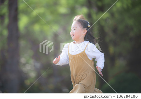一個快樂的孩子，捕捉女孩在綠樹成蔭的公園裡活力四射地奔跑時臉上洋溢的笑容和純真。 136294190