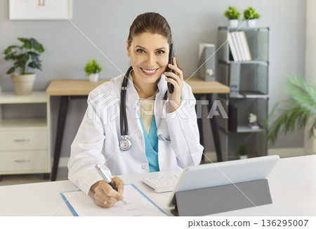 Young woman therapist in coat consulting patient remotely by phone call 136295007