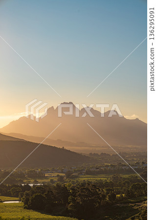 Majestic mountain range at golden hour. Panoramic view of a rural valley with lush vineyards under a clear sky. Nature landscape for travel. Majestic mountain range at golden hour. Panoramic view of a rural valley with lush vineyards under a clear sky. Nature landscape for travel. 136295091