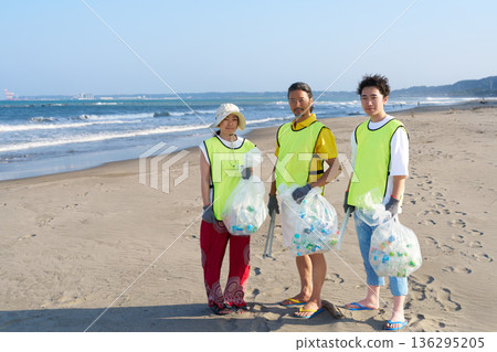 Three male and female volunteer staff members participating in beach cleanup volunteer activities 136295205