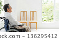 A back view of a senior man in a wheelchair looking out a bright window. An image of a peaceful and secure retirement in a nursing home or at home. 136295412