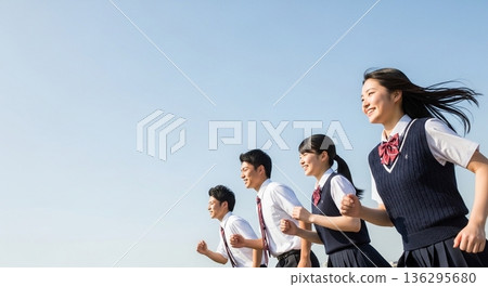 Four high school boys and girls running with smiles under the blue sky. With a wide margin on the left, this advertising material evokes the image of youth and the future. Four high school boys and girls running with smiles under the blue sky. With a wide margin on the left, this advertising material evokes the image of youth and the future. 136295680