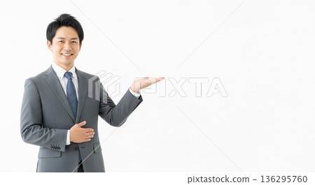 A smiling male business person in a suit giving directions. A versatile advertising image with ample white space on the right. 136295760