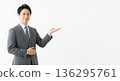A smiling male business person in a suit giving directions. A versatile advertising image with ample white space on the right. 136295761