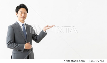 A smiling male business person in a suit giving directions. A versatile advertising image with ample white space on the right. 136295761