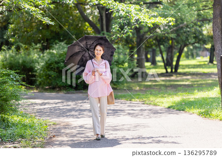一位面帶微笑的女士撐著陽傘行走。 一位面帶微笑的女士撐著陽傘行走。 136295789