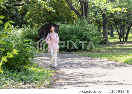 一位面帶微笑的女士撐著陽傘行走。 136295848