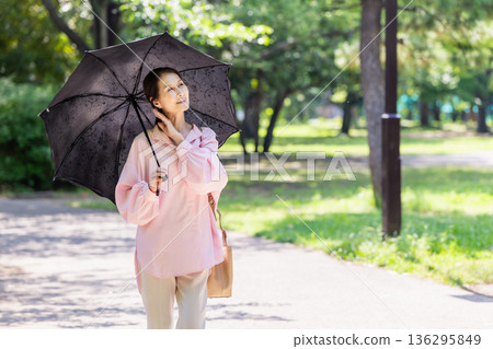 一位面帶微笑的女士撐著陽傘行走。 一位面帶微笑的女士撐著陽傘行走。 136295849
