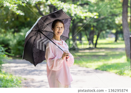 一位面帶微笑的女士撐著陽傘行走。 136295874