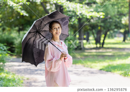一位面帶微笑的女士撐著陽傘行走。 136295876
