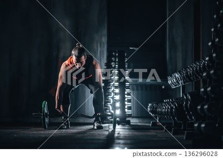 Male bodybuilder preparing barbell deadlift near dumbbell rack in gym, Man training with barbell for strength in fitness gym with dumbbell stand Male bodybuilder preparing barbell deadlift near dumbbell rack in gym, Man training with barbell for strength in fitness gym with dumbbell stand 136296028