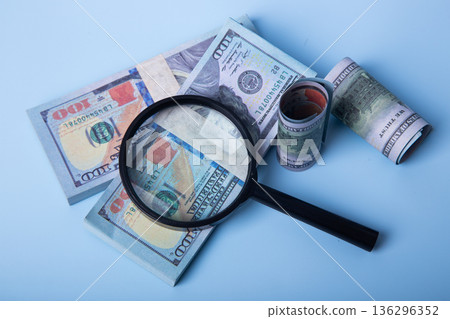 Magnifying glass inspecting us dollar bills on blue background 136296352