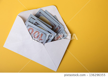 Hundred dollar bills in white envelope on yellow background Hundred dollar bills in white envelope on yellow background 136296355