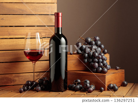 Bottle and glass of red wine and blue grapes on a wooden background. Bottle and glass of red wine and blue grapes on a wooden background. 136297251