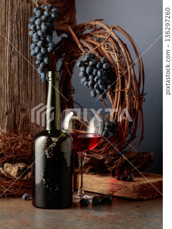 An antique bottle of port wine against the backdrop of an old weathered board, dried vine, and blue grapes. An antique bottle of port wine against the backdrop of an old weathered board, dried vine, and blue grapes. 136297260