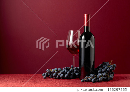 Bottle and glass of red wine with blue grapes on a red background. 136297265
