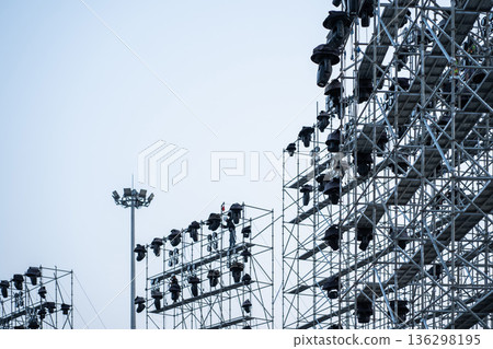 construction workers assembling large scaffolding and metal rigs for outdoor event concert, professional stage light equipment construction 136298195