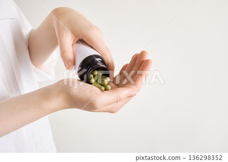 Women's hands pouring green capsules from bottle, representing health supplements and wellness 136298352