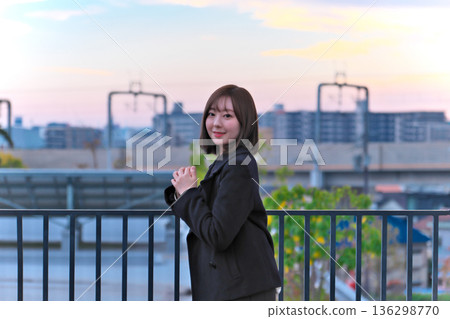 黃昏時分,一位身著冬裝的日本女子麵帶微笑,背景是鐵軌和城市景觀。 黃昏時分,一位身著冬裝的日本女子麵帶微笑,背景是鐵軌和城市景觀。 136298770