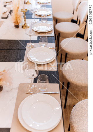 Elegant banquet table setting with white plates, glassware and neutral modern seating Elegant banquet table setting with white plates, glassware and neutral modern seating 136298772