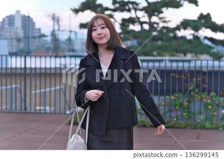 A female university student (Japanese woman) in winter clothes standing on the rooftop with her bag. An image of commuting to school, going out, and starting a new life. A female university student (Japanese woman) in winter clothes standing on the rooftop with her bag. An image of commuting to school, going out, and starting a new life. 136299145