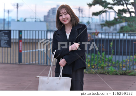 A female university student (Japanese woman) in winter clothes standing on the rooftop with her bag. An image of commuting to school, going out, and starting a new life. A female university student (Japanese woman) in winter clothes standing on the rooftop with her bag. An image of commuting to school, going out, and starting a new life. 136299152
