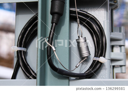 Black electrical cable and metal security lock attached to an outdoor utility box. Electrical wiring and safety for industrial infrastructure concept. 136299381