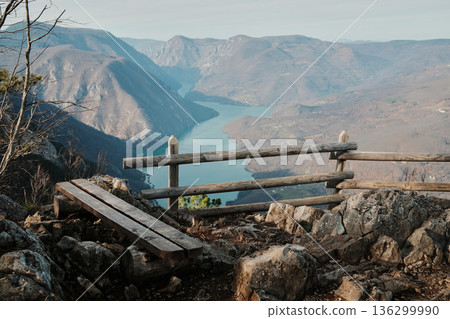 Wooden bench and fence on rocky viewpoint overlooking Drina River canyon and Perucac Lake in Tara National Park, Serbia. Mountain landscape with steep slopes and water Wooden bench and fence on rocky viewpoint overlooking Drina River canyon and Perucac Lake in Tara National Park, Serbia. Mountain landscape with steep slopes and water 136299990