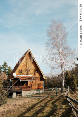 A frame wooden cabin standing on open meadow near forest in Tara National Park, Serbia. Minimal mountain housing under clear sky A frame wooden cabin standing on open meadow near forest in Tara National Park, Serbia. Minimal mountain housing under clear sky 136300016