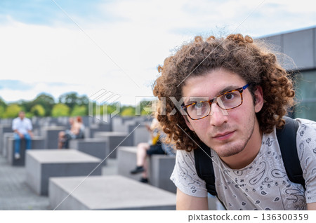 Berlin, germany, august 12, 2023. Young man with curly hair and glasses looking at the camera, standing in the memorial to the murdered jews of europe in berlin Berlin, germany, august 12, 2023. Young man with curly hair and glasses looking at the camera, standing in the memorial to the murdered jews of europe in berlin 136300359